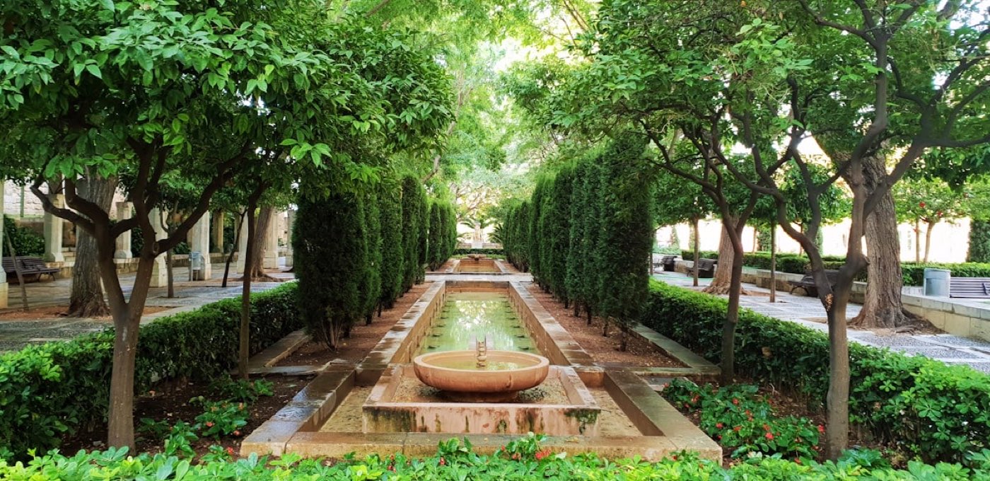 A formal Mediterranean garden with a stone fountain and cypress avenue