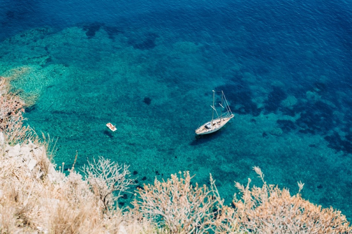 An aerial view of a sailing yacht crossing turquoise Mediterranean water